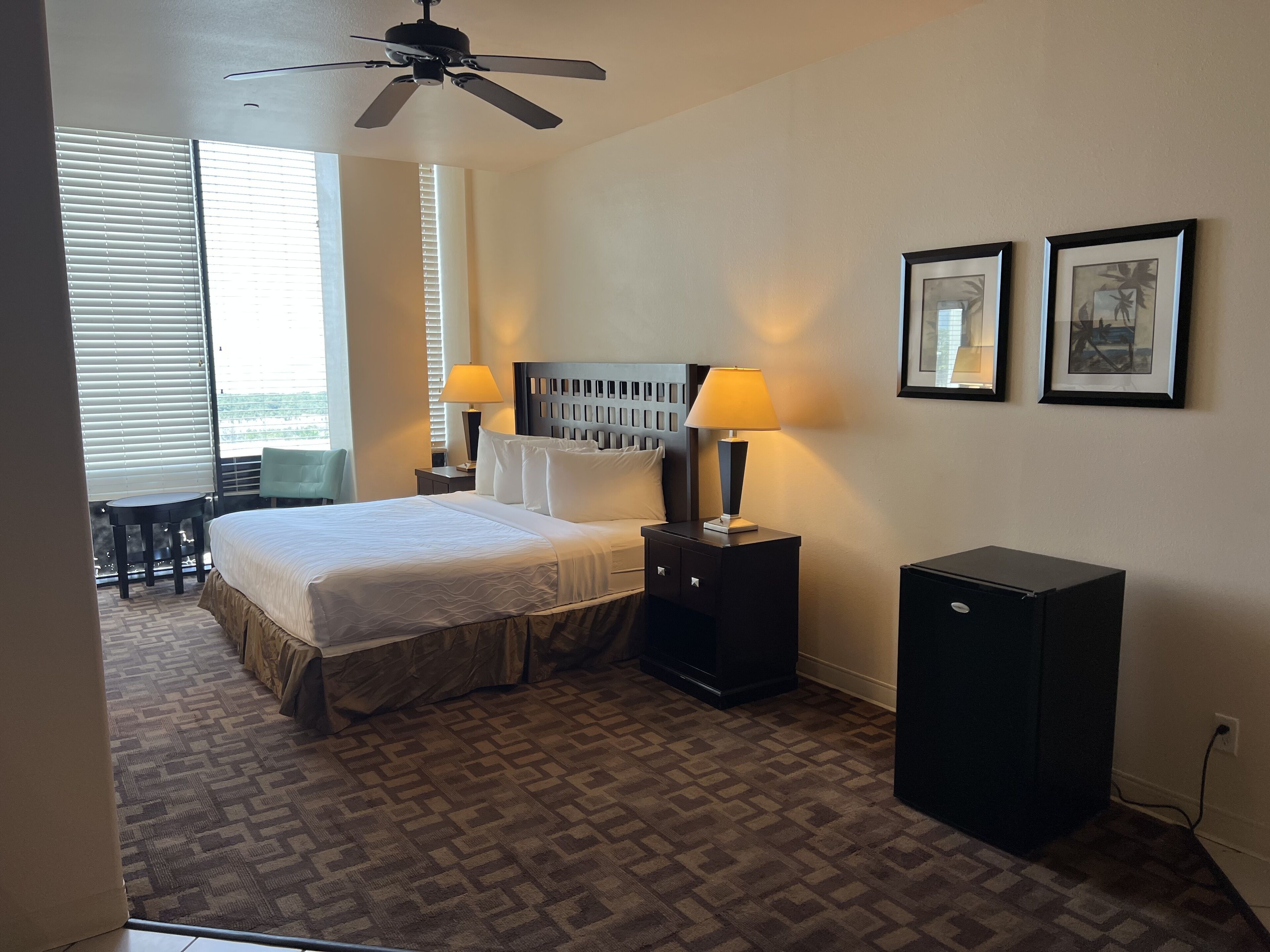 A hotel room with a bed, two bedside tables, a ceiling fan, a desk, a chair, and a small cabinet.