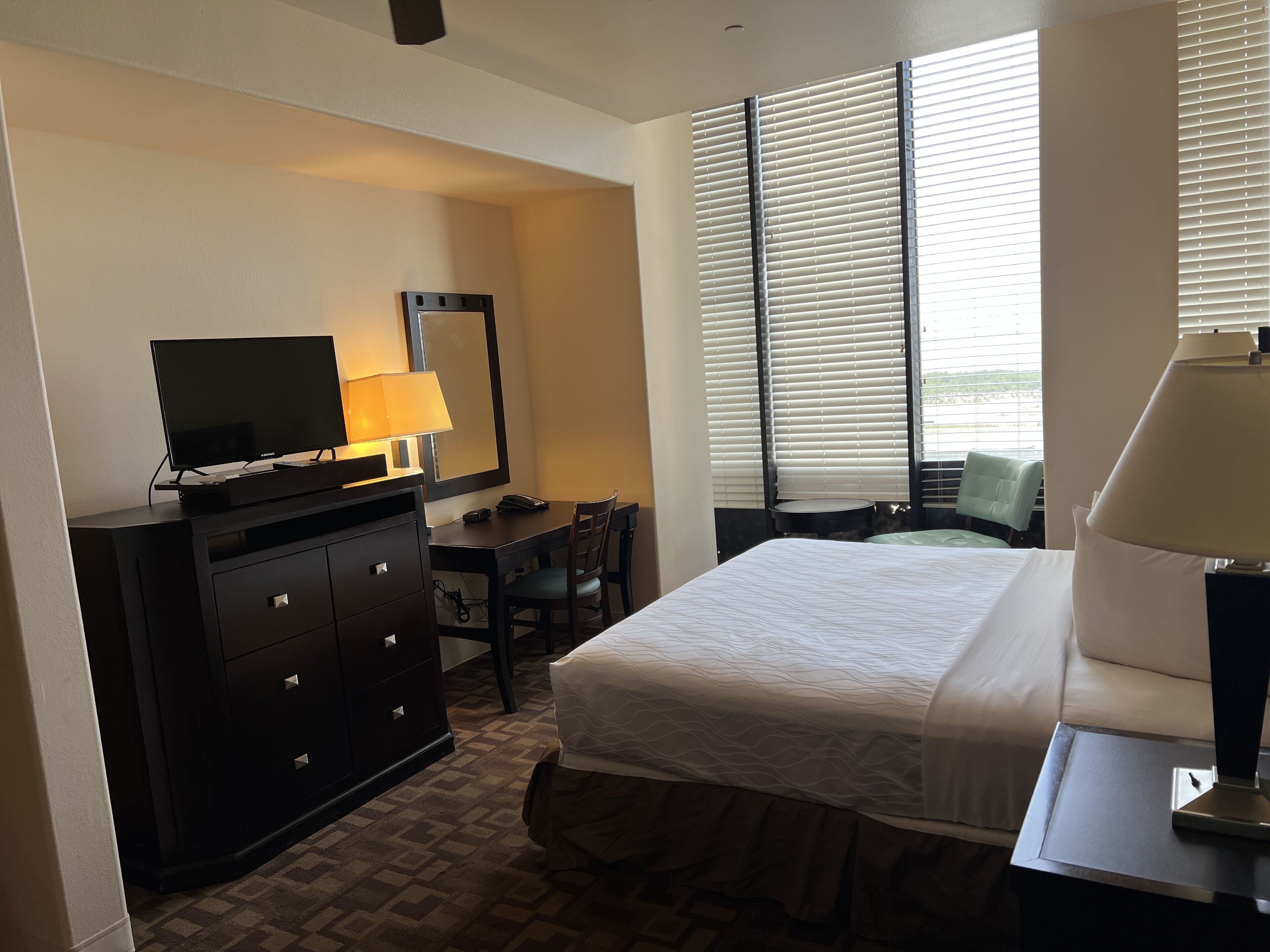 Una habitación de hotel con una cama, un escritorio con lámpara, un televisor y una silla.