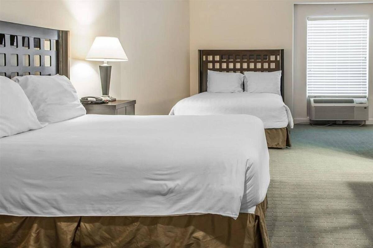 A hotel room with two beds, a nightstand with a lamp, and an air conditioning unit.