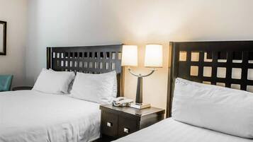 A hotel room with two beds, each with a wooden headboard, white bedding, and a bedside table with a lamp and a phone.
