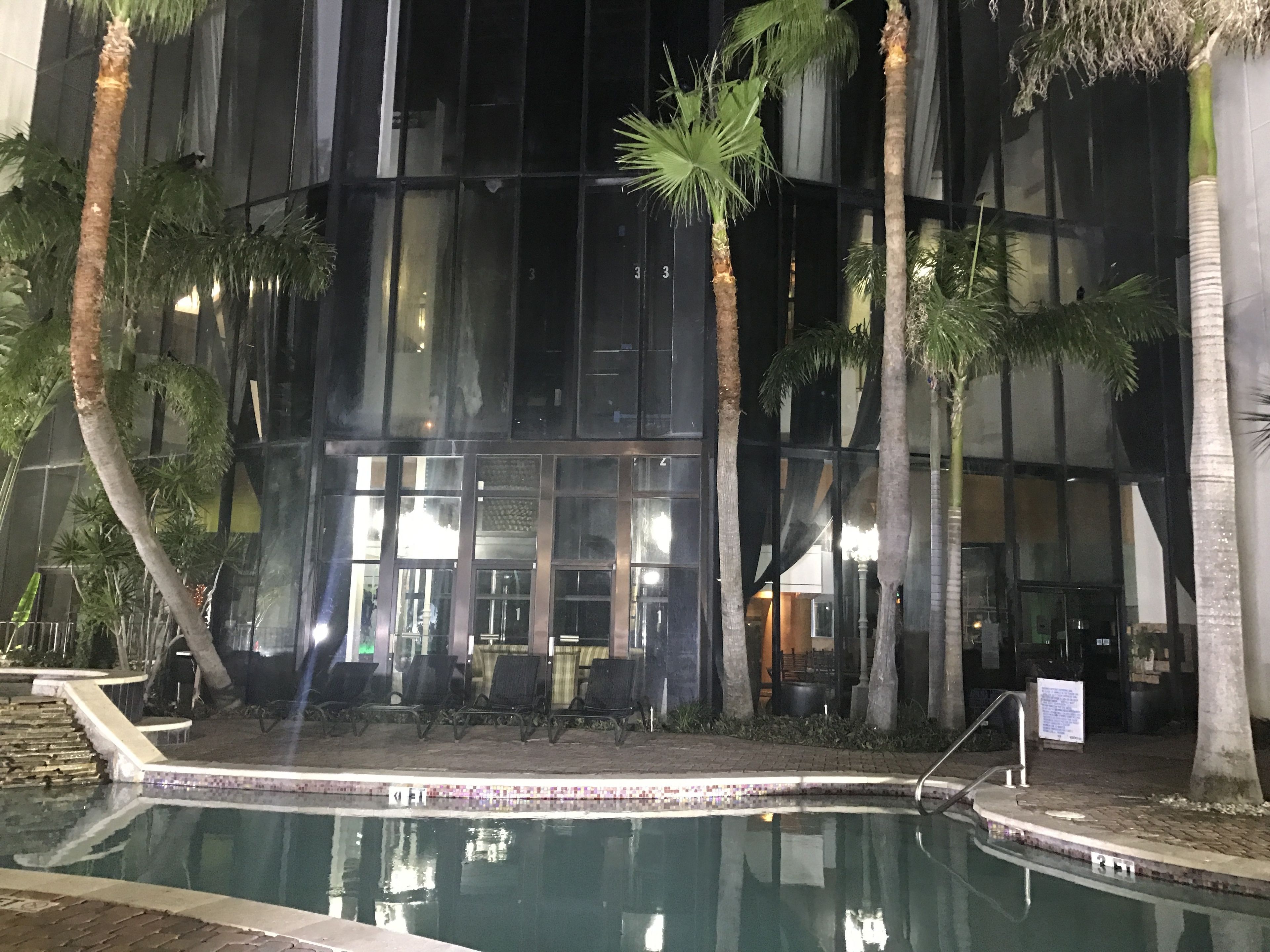 Vue nocturne d’un bâtiment doté d’une piscine, de palmiers et d’un espace de détente extérieur.