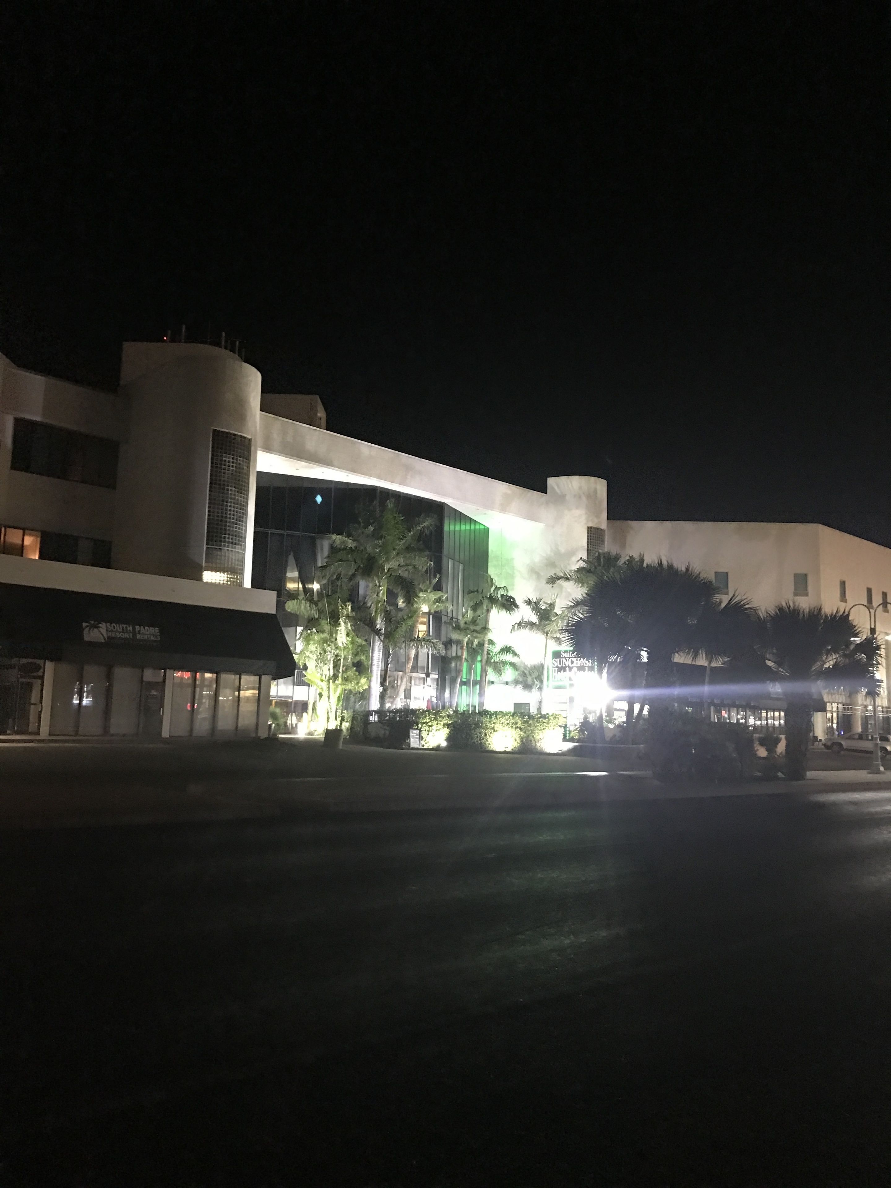 Un edificio moderno con fachada curva, ventanas amplias y entrada iluminada en verde.