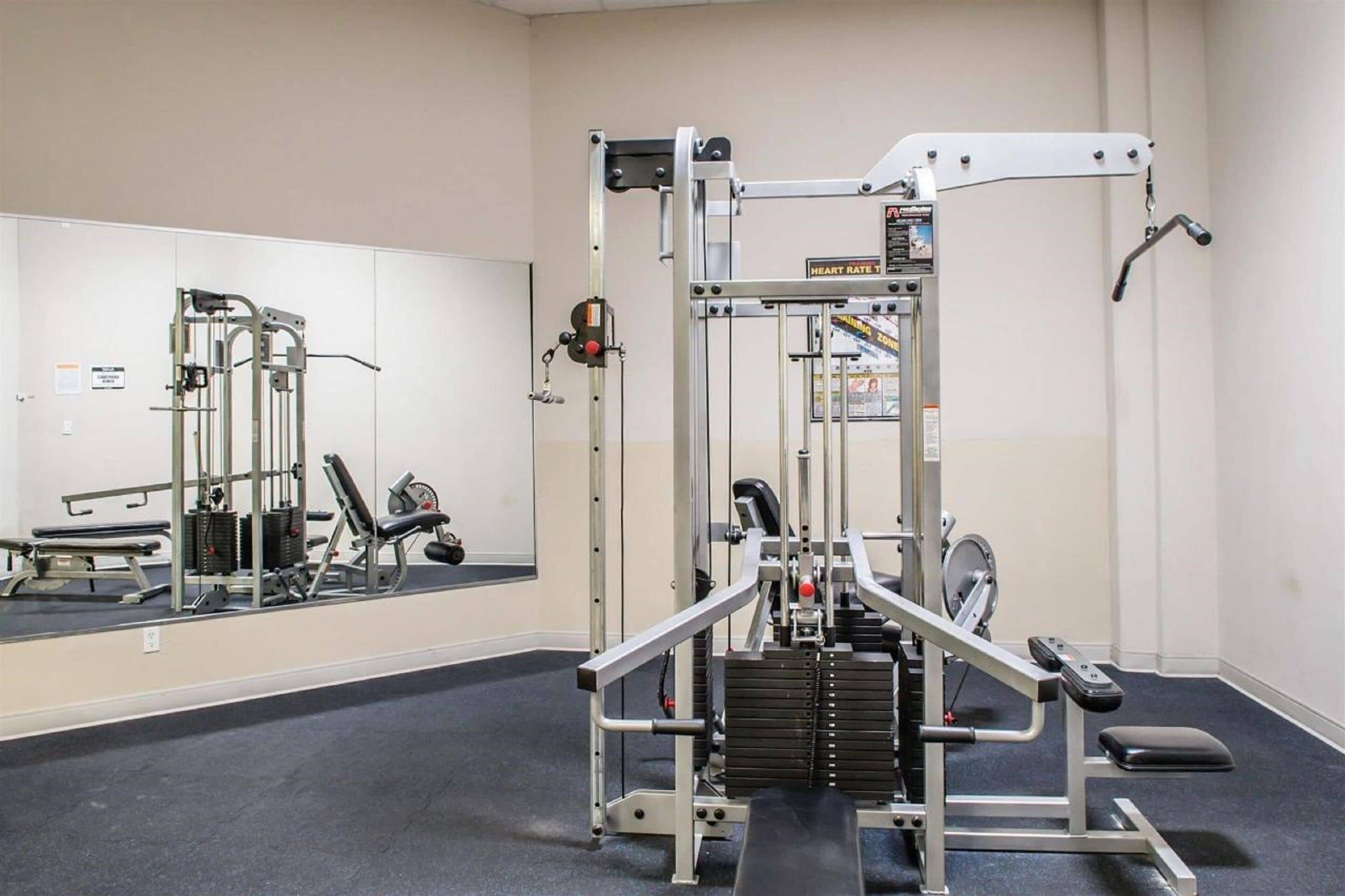 Ein Fitnessstudio mit Spiegelwand, Kraftgeräten und einer Bank.