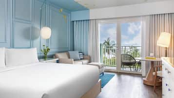 A hotel room with a large bed, a sofa, a dining table, and a balcony with a view.