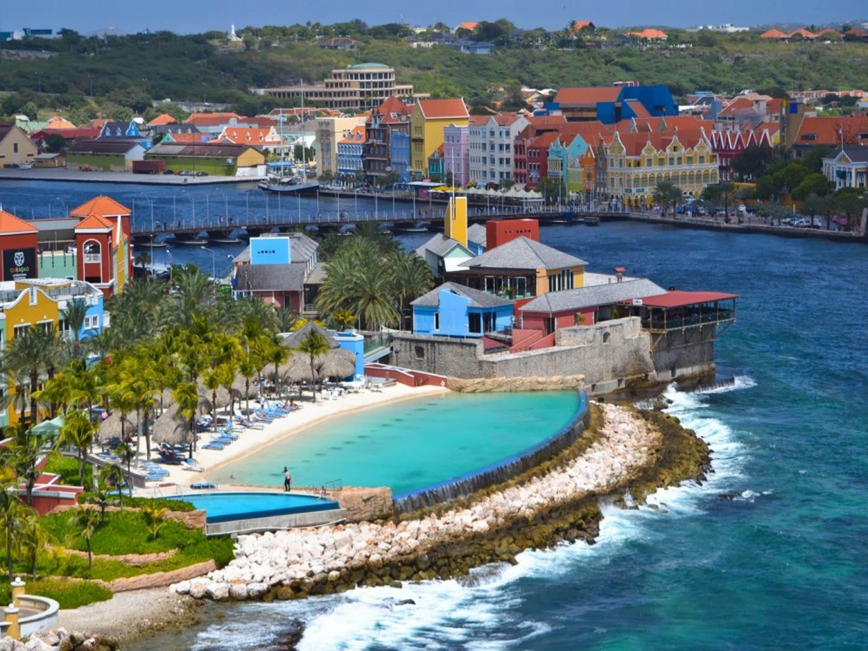 A coastal resort with colorful buildings, a beach, and a rocky breakwater.