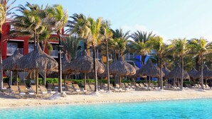 A beach resort with thatched umbrellas, lounge chairs, and palm trees. - Renaissance Wind Creek Curacao Resort (Willemstad)