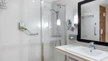 Un baño moderno con ducha envuelta en vidrio, un lavamanos blanco y un espejo grande.