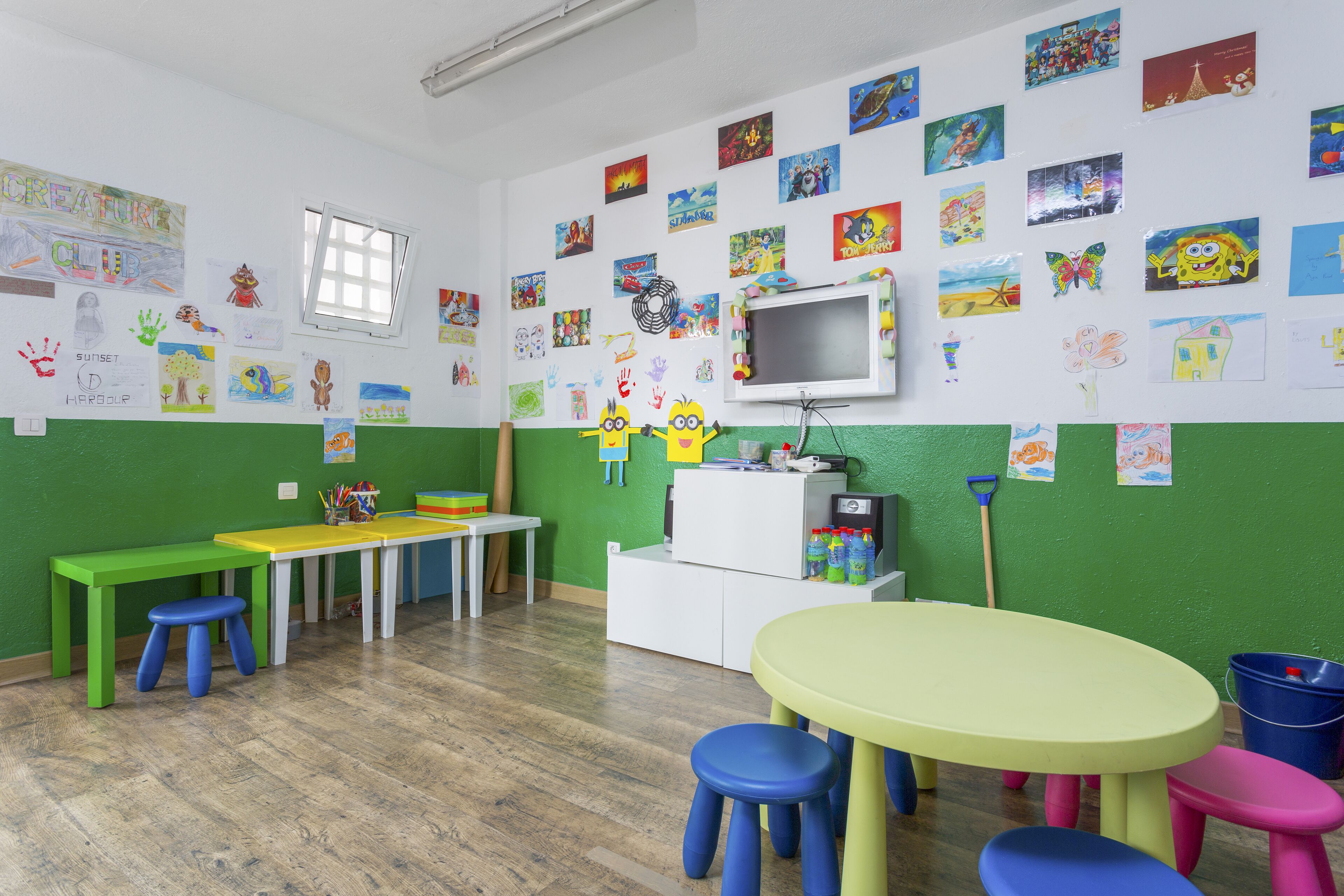 A classroom with green walls, a whiteboard, a television, and various children's artwork.