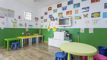 Een klaslokaal met groene wanden, een whiteboard, een televisie en diverse kinderwerken.