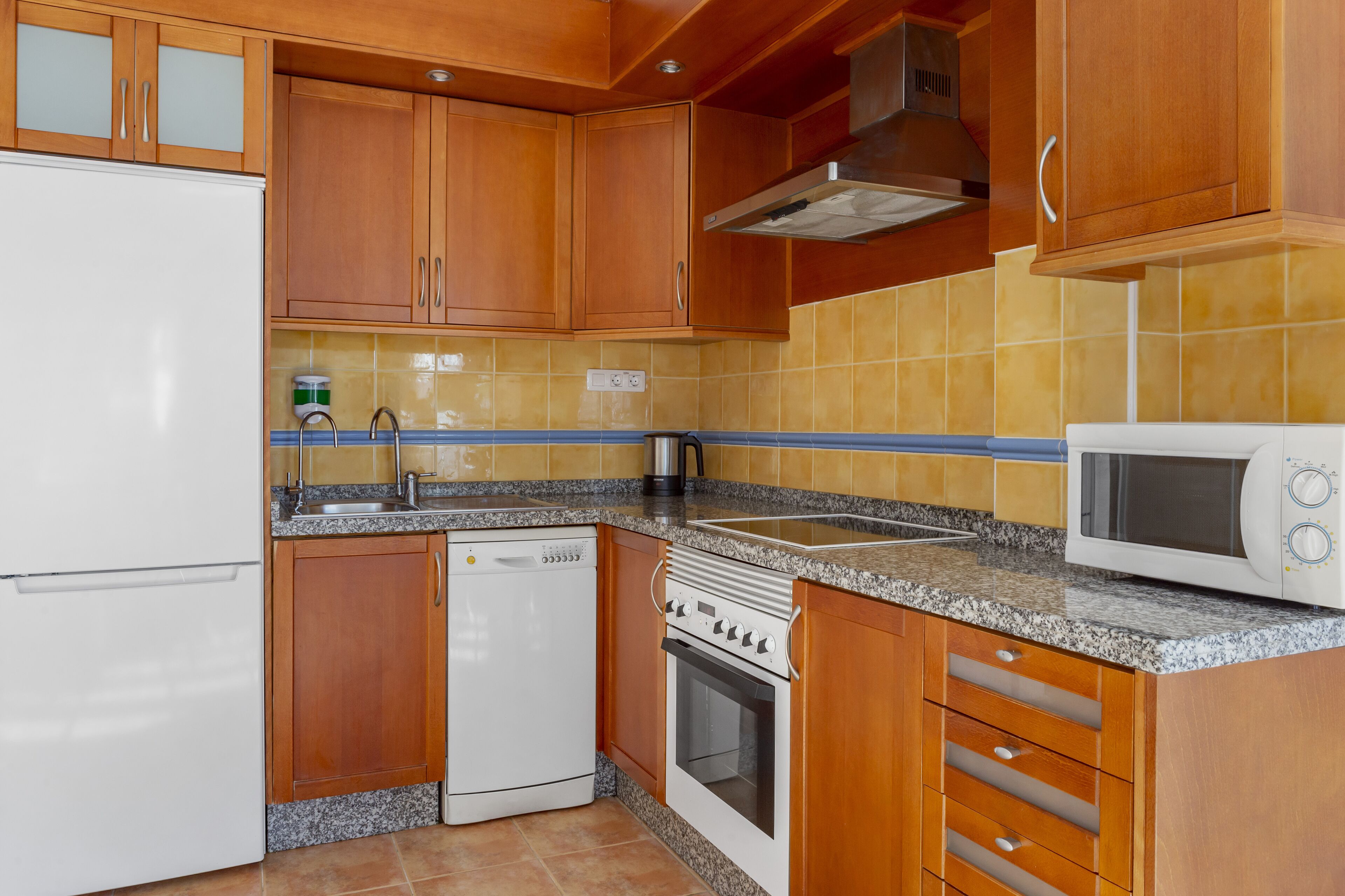 A compact kitchen with wooden cabinets, a built-in oven, a dishwasher, and a microwave.