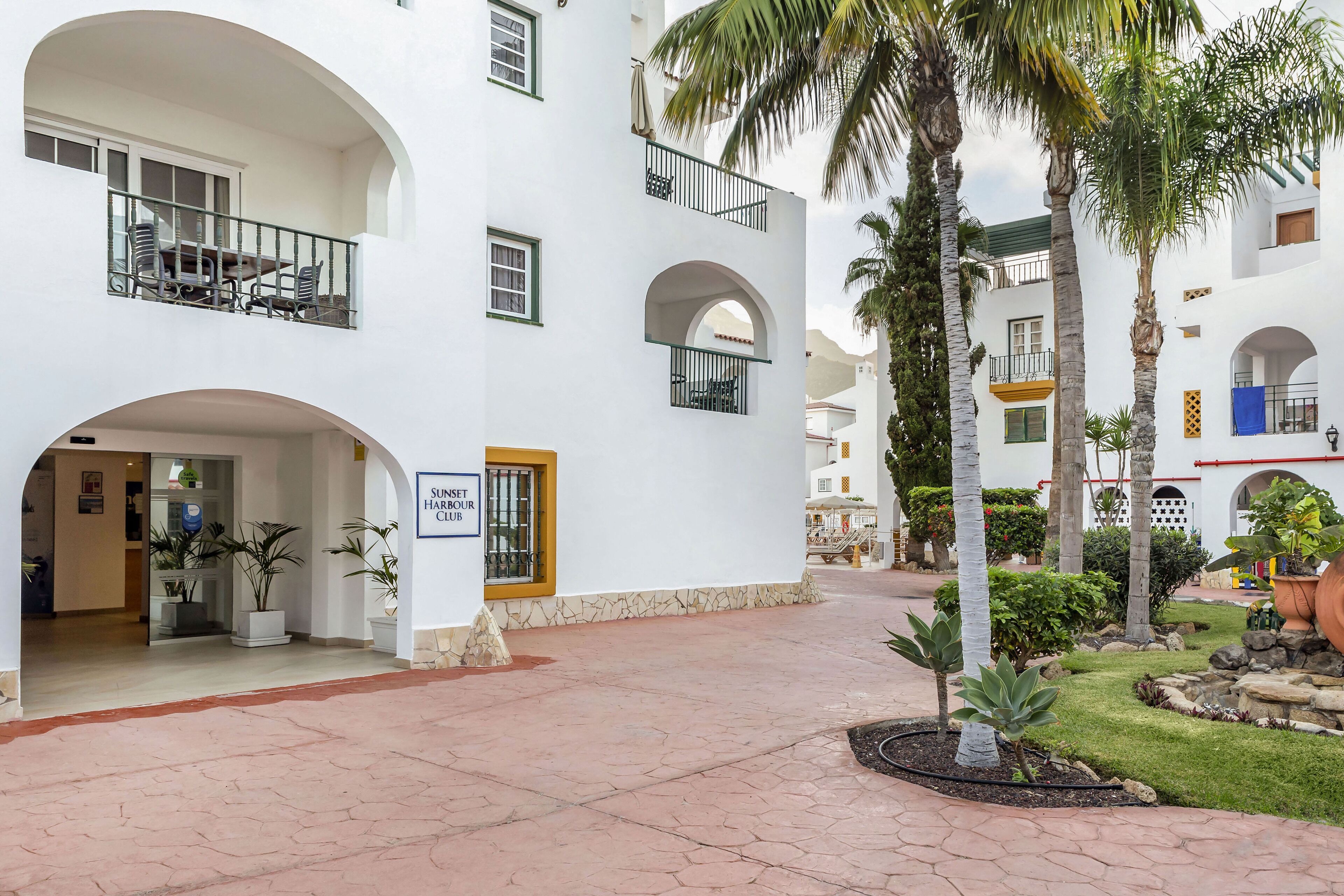 A hotel courtyard with a pool, palm trees, and a sign for the Sunset Hour Club.