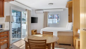A hotel room with a bed, a dining table with chairs, a TV, and a sliding glass door to the balcony.