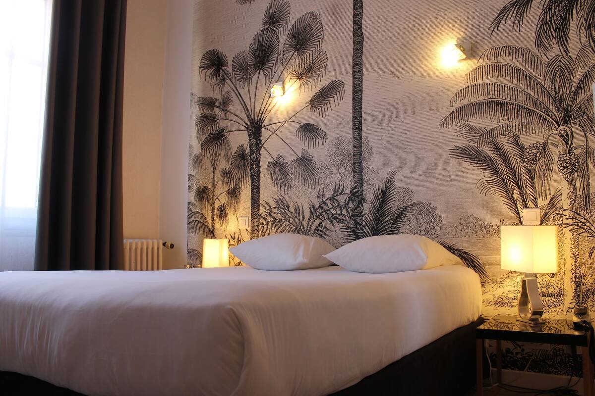 A hotel room with a large bed, two bedside lamps, and a wall mural of palm trees.