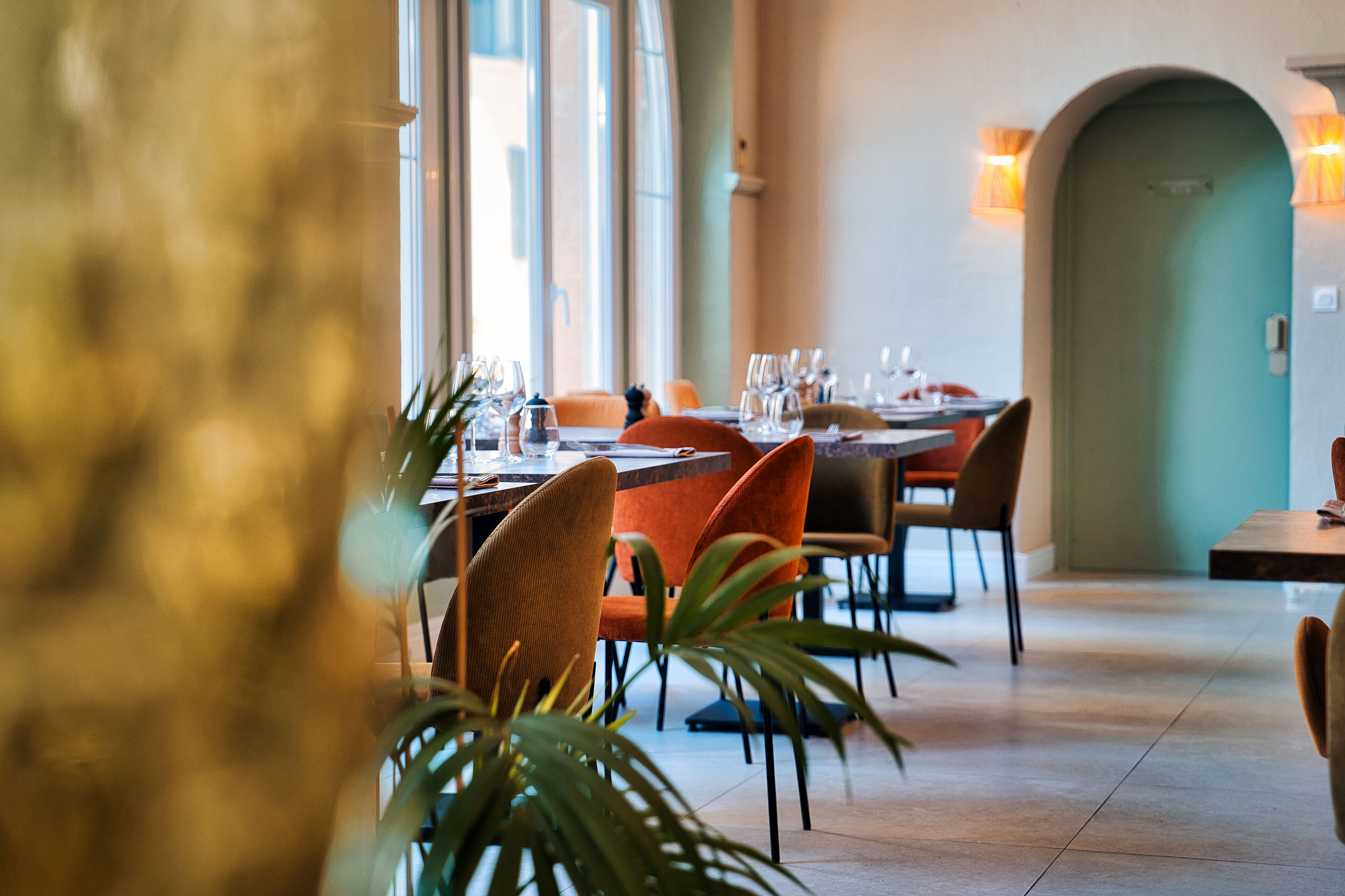 A restaurant with tables set for dining, chairs, and potted plants.