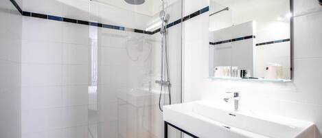 A modern bathroom with a glass shower enclosure, a white sink, and a mirror above it.