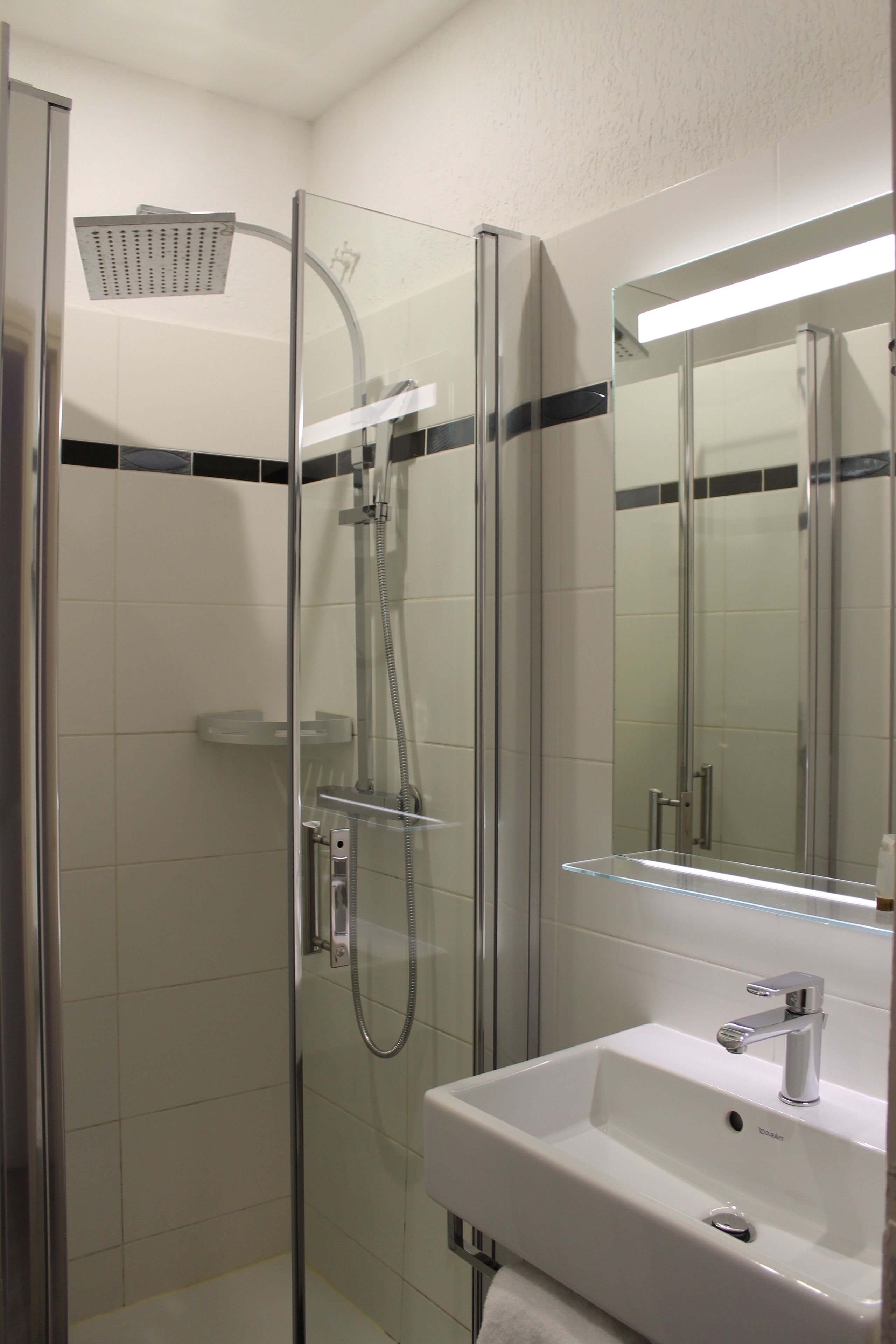 A modern bathroom with a glass-enclosed shower, a white sink, and a mirror with integrated lighting.