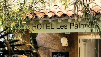 Señal de HOTEL Les Palmieres, con techo de tejas rústico y una puerta a la derecha.