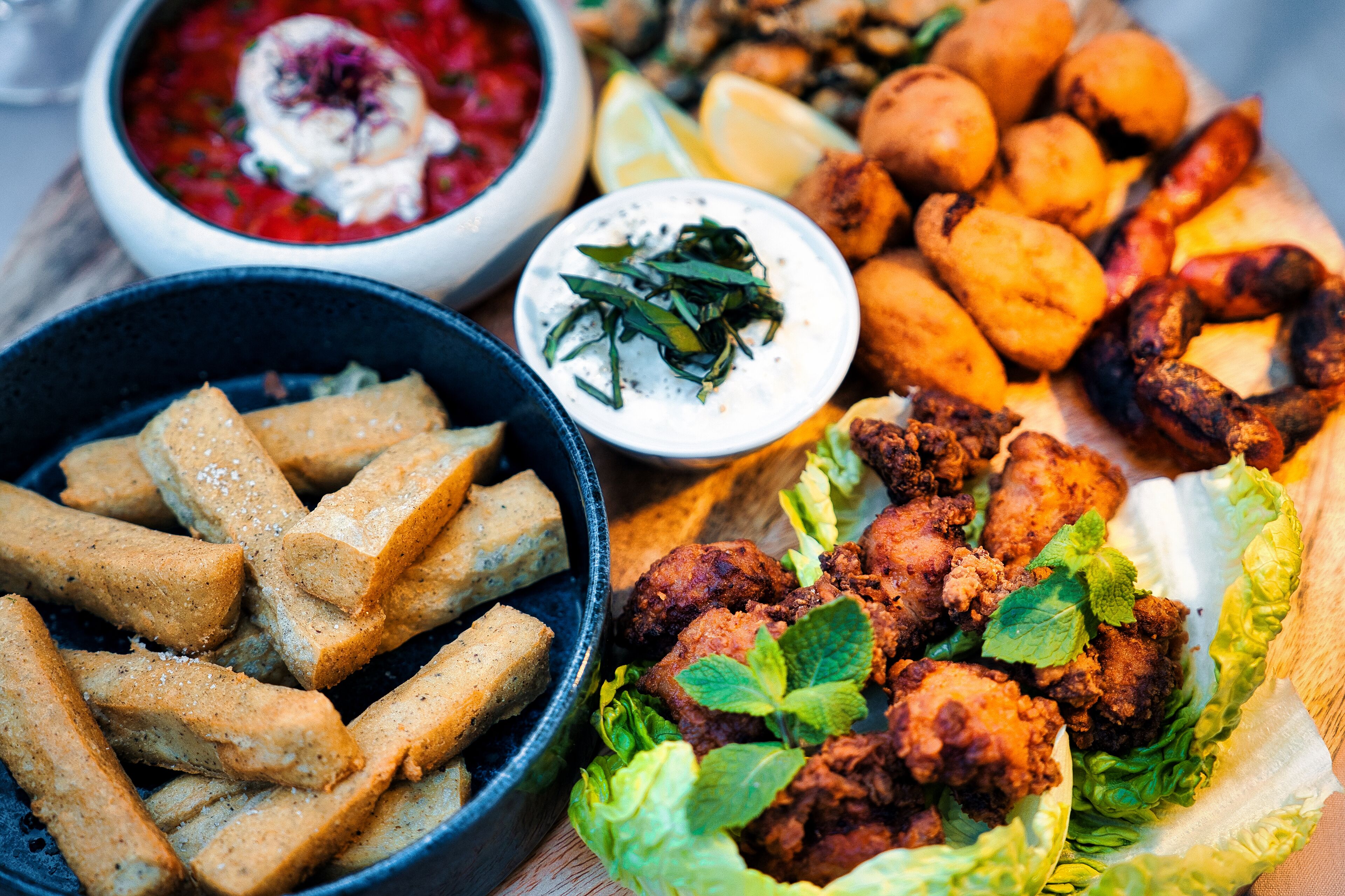 A variety of fried foods including fried chicken, fries, and fried dough sticks, served with dipping sauces and garnishes.