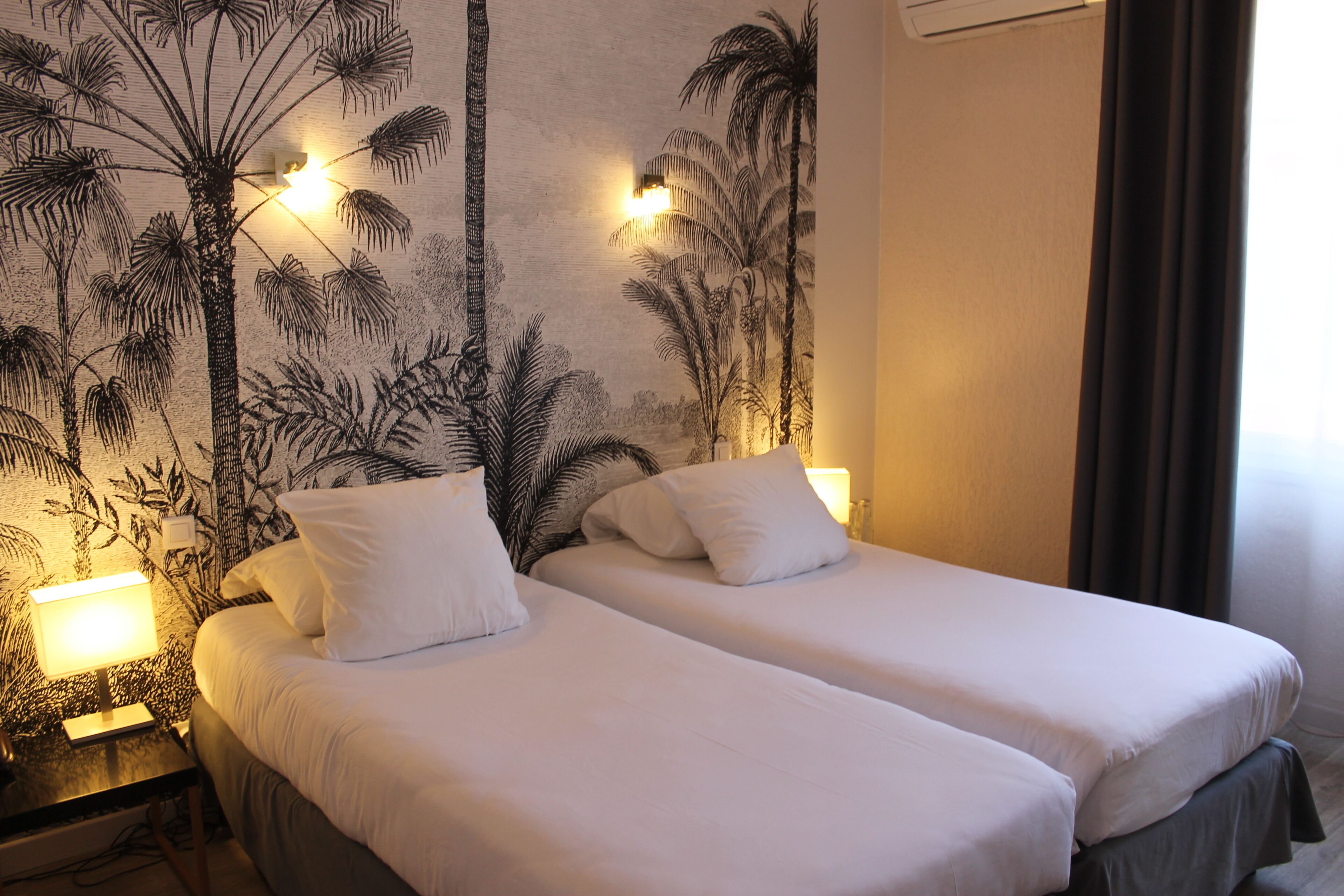 Une chambre avec deux lits, une fresque murale représentant des palmiers et des lampes de chevet.