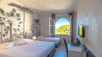 Habitación de hotel con dos camas, un escritorio con lámpara, televisión y ventana con vistas a zonas verdes.