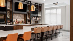 Uma área de bar moderna com um balcão extenso, vários bancos altos e uma variedade de garrafas e copos.