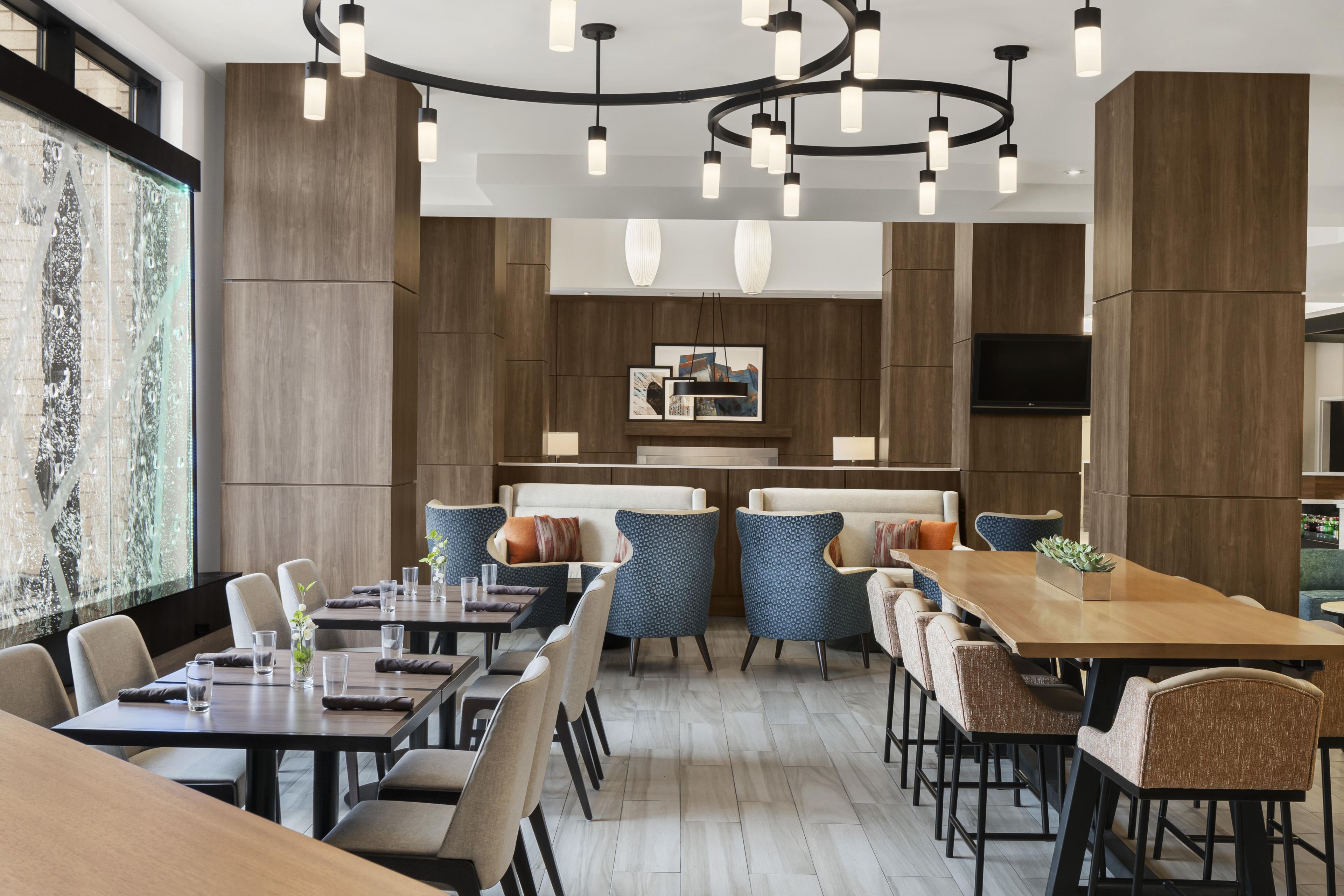 Un comedor moderno con varias mesas y sillas, un área de estar central con sofás, y un ventanal con vistas.