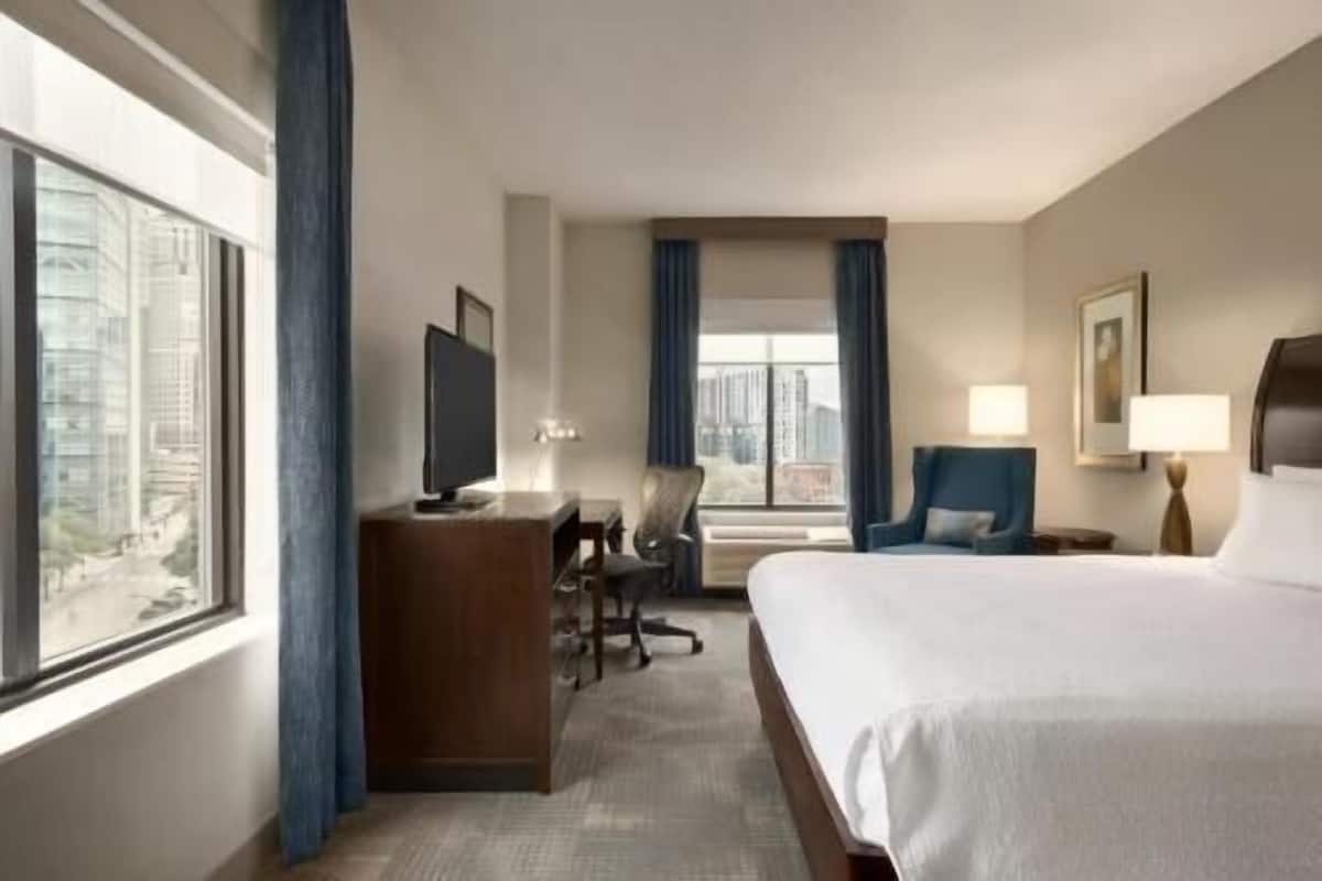 Habitación de hotel con cama, escritorio con computadora, silla y ventana con cortinas.