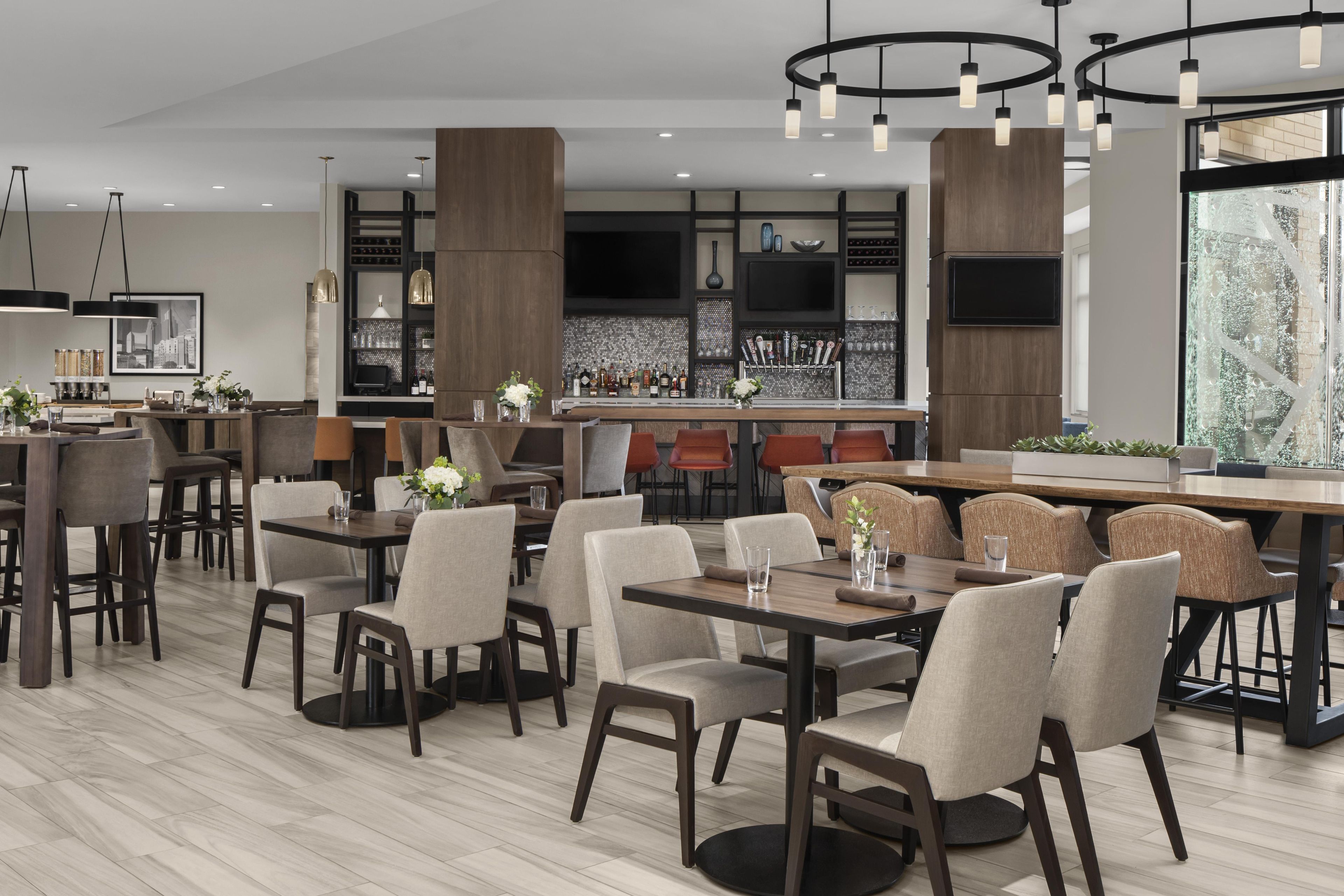 Un restaurante moderno con mesas altas, sillas, una zona de bar y un ventanal grande.