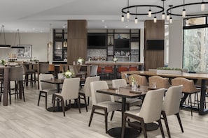 Un restaurante moderno con mesas altas, sillas, una zona de bar y un ventanal grande.