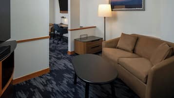 Habitación de hotel con sofá, una mesita, escritorio con silla, lámpara y un cuadro en la pared.