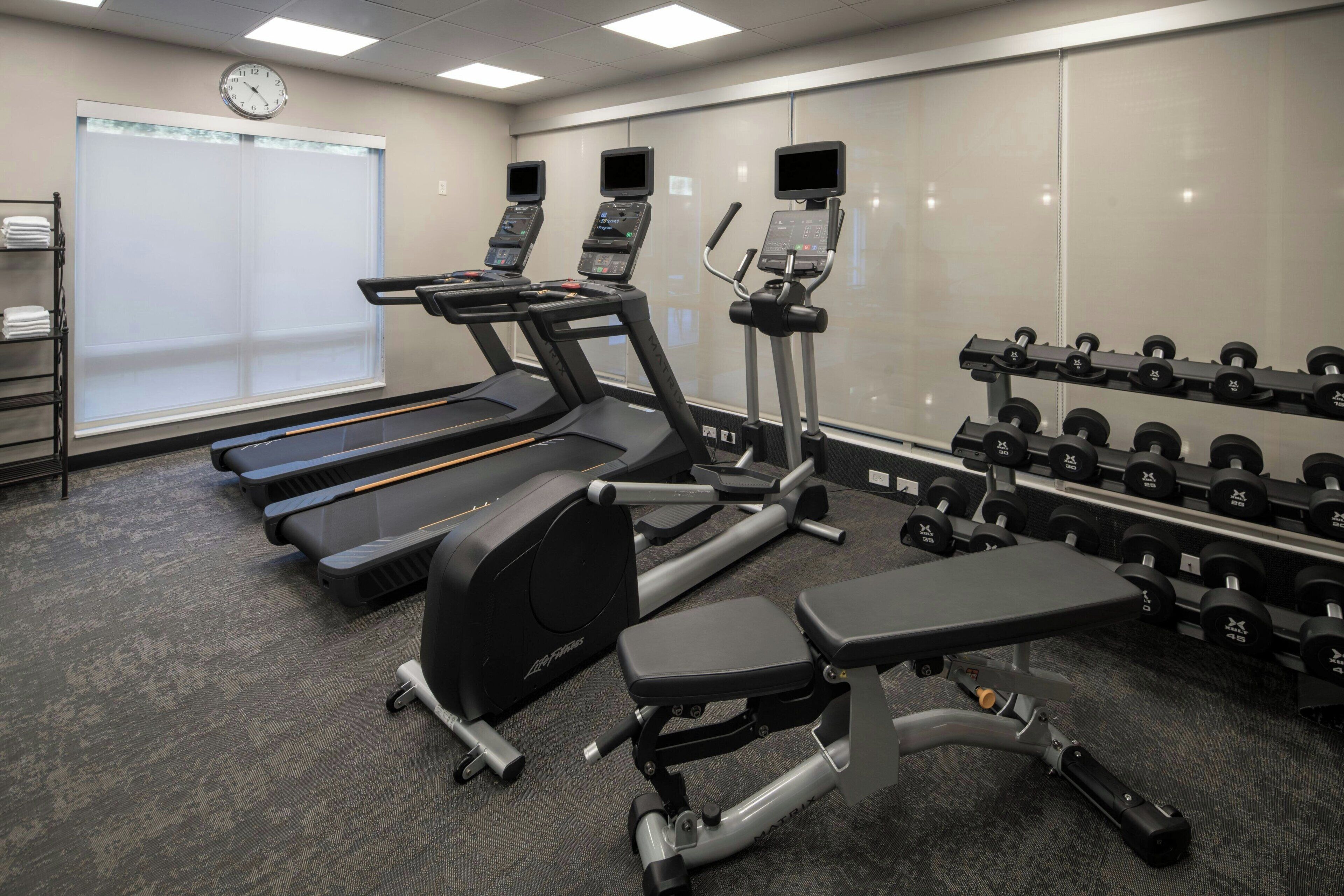 Een fitnessruimte met loopbanden, een elliptische machine, een bankdrukrek en een rek met dumbbells.