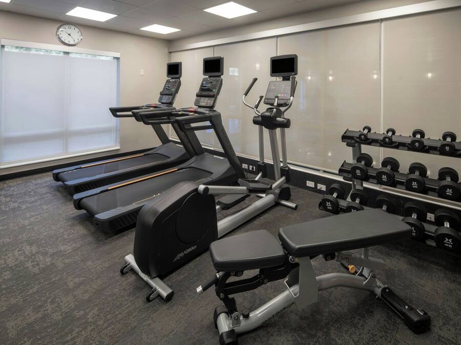 Een fitnessruimte met loopbanden, een elliptische machine, een bankdrukrek en een rek met dumbbells.