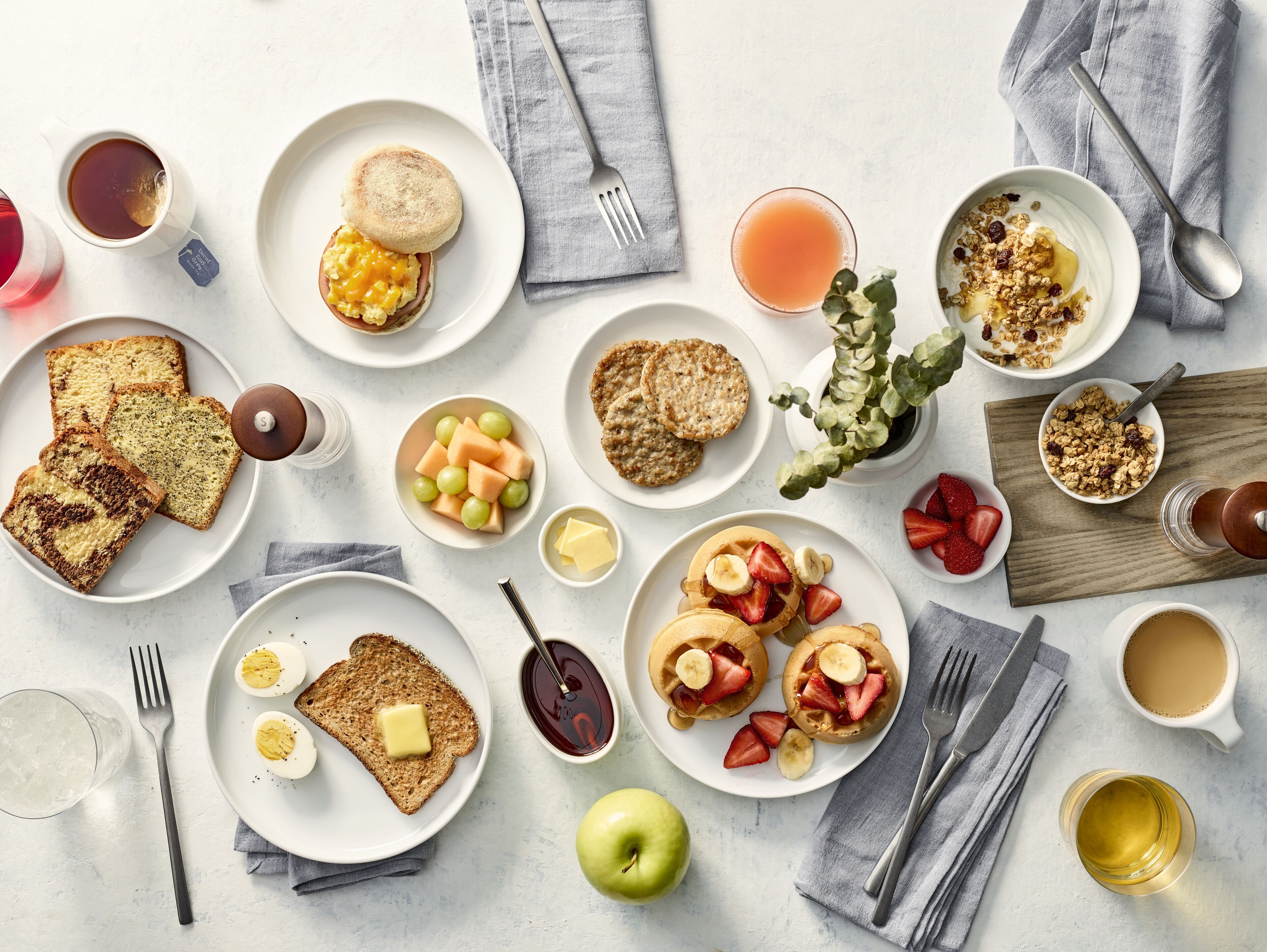 A breakfast spread with toast, eggs, pancakes, and various fruits and beverages.