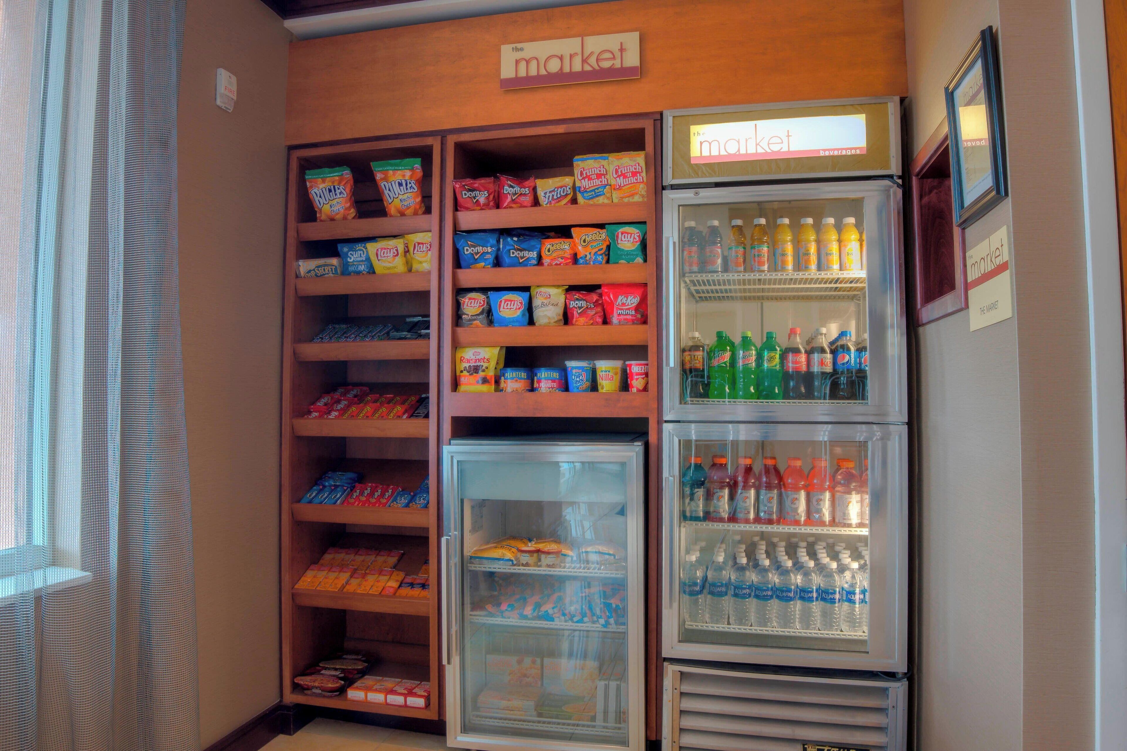 Un área de venta de aperitivos y bebidas con varios estantes llenos de papas fritas, botanas y bebidas embotelladas.