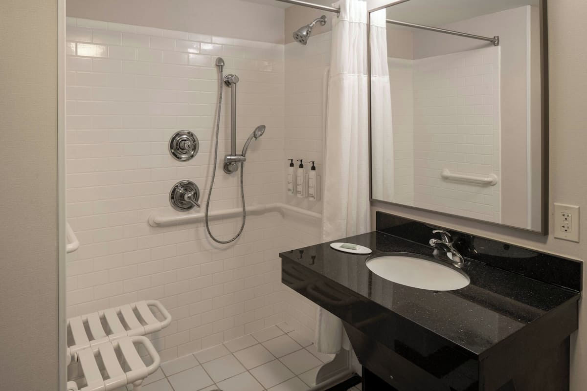 ルーム キングベッド 1 台 聴覚に障がいのある方に対応 (Roll-in Shower & Transfer Shower) | バスルーム | シャワー付き浴槽、デザイナーバスアメニティ、ヘアドライヤー、タオル