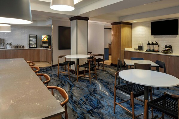 A modern hotel lobby with a long reception desk, multiple seating areas, a flat-screen TV, and a bar area with a white-tiled backsplash.