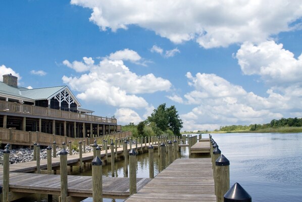 A wooden pier extending into calm water, with a building featuring a green roof and a deck on the left.