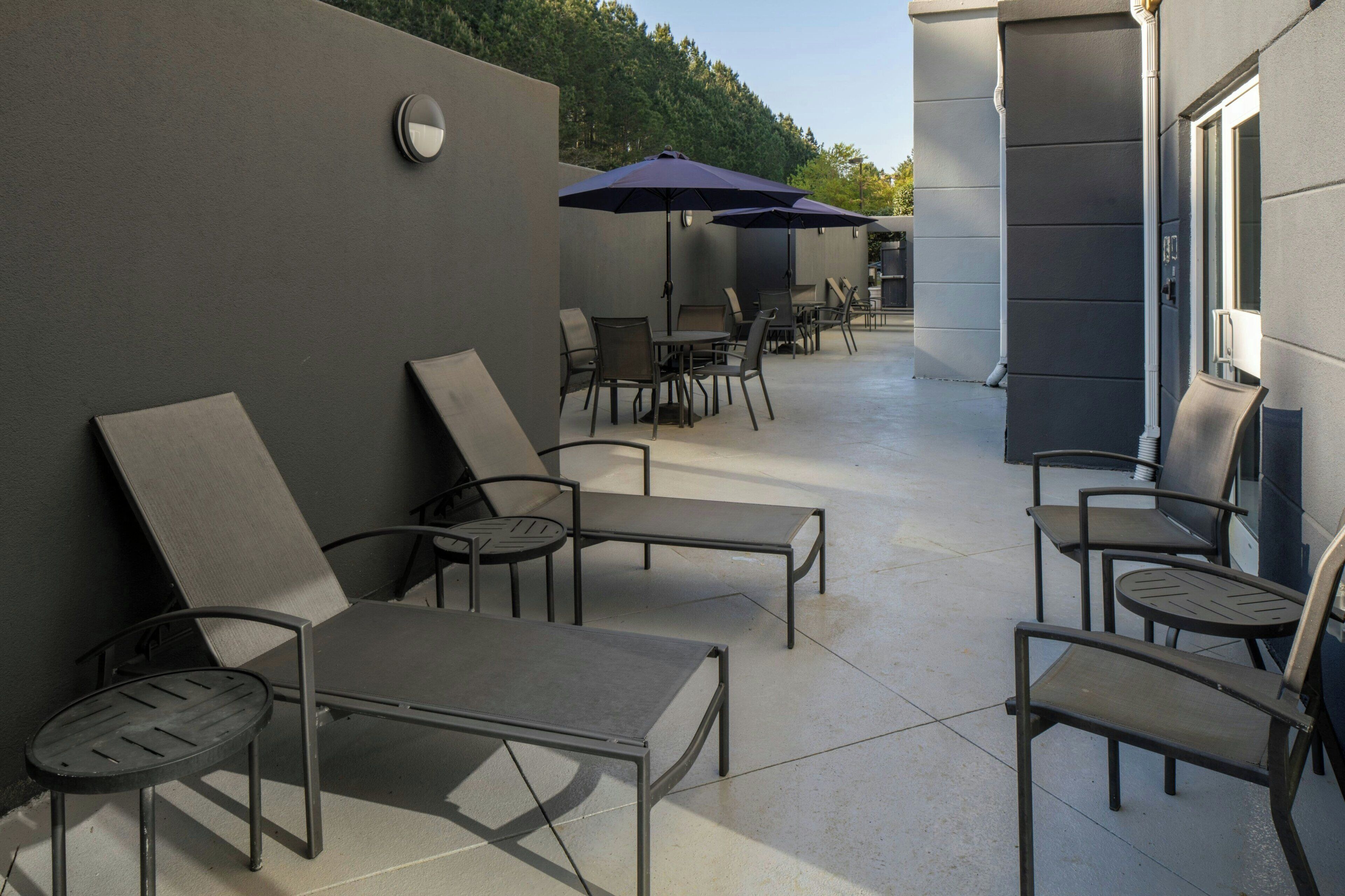 An outdoor patio area with lounge chairs and tables, umbrellas, and a wall-mounted light fixture.