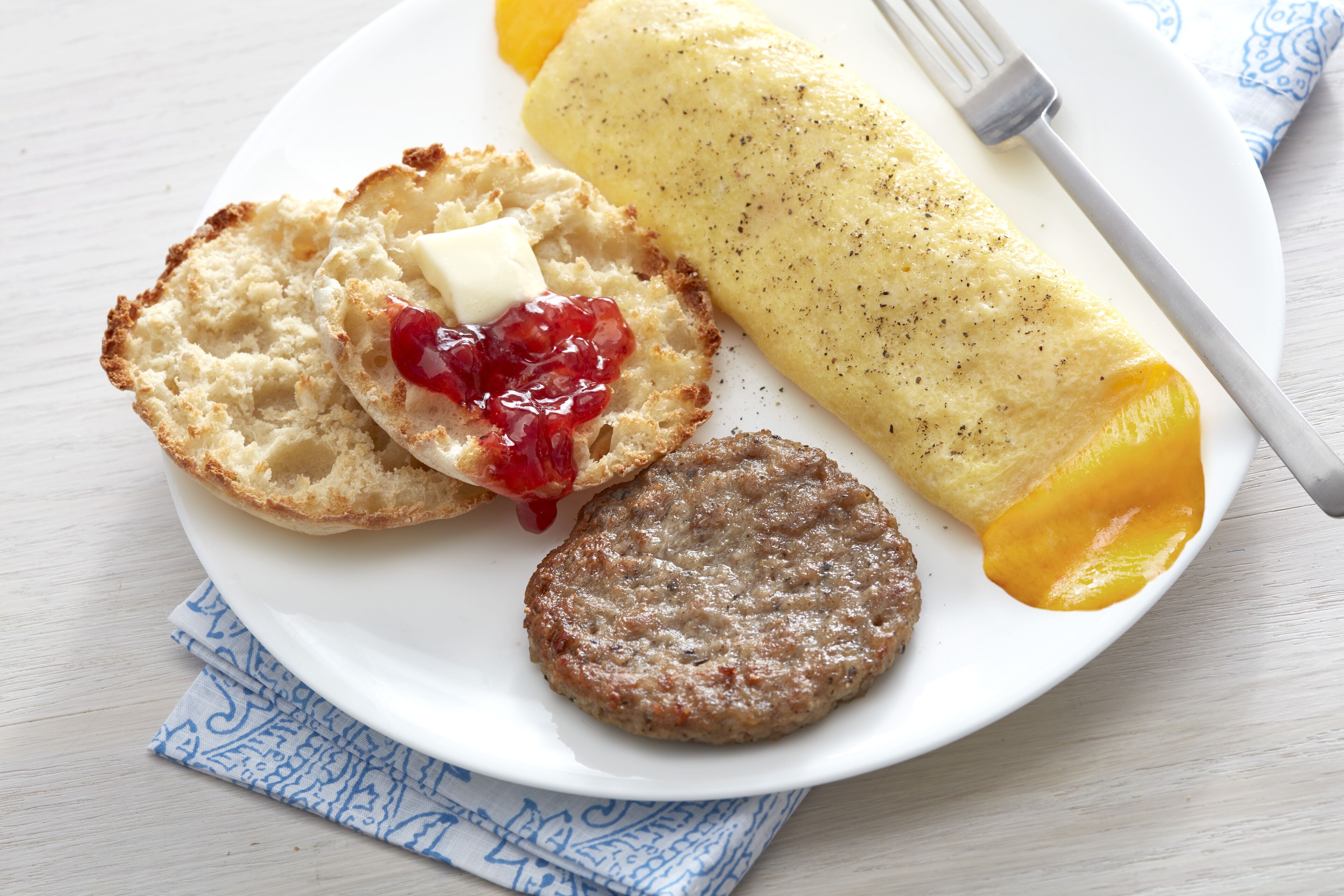 A plate with a rolled omelette, two pieces of toast with butter and jam, and a sausage patty.