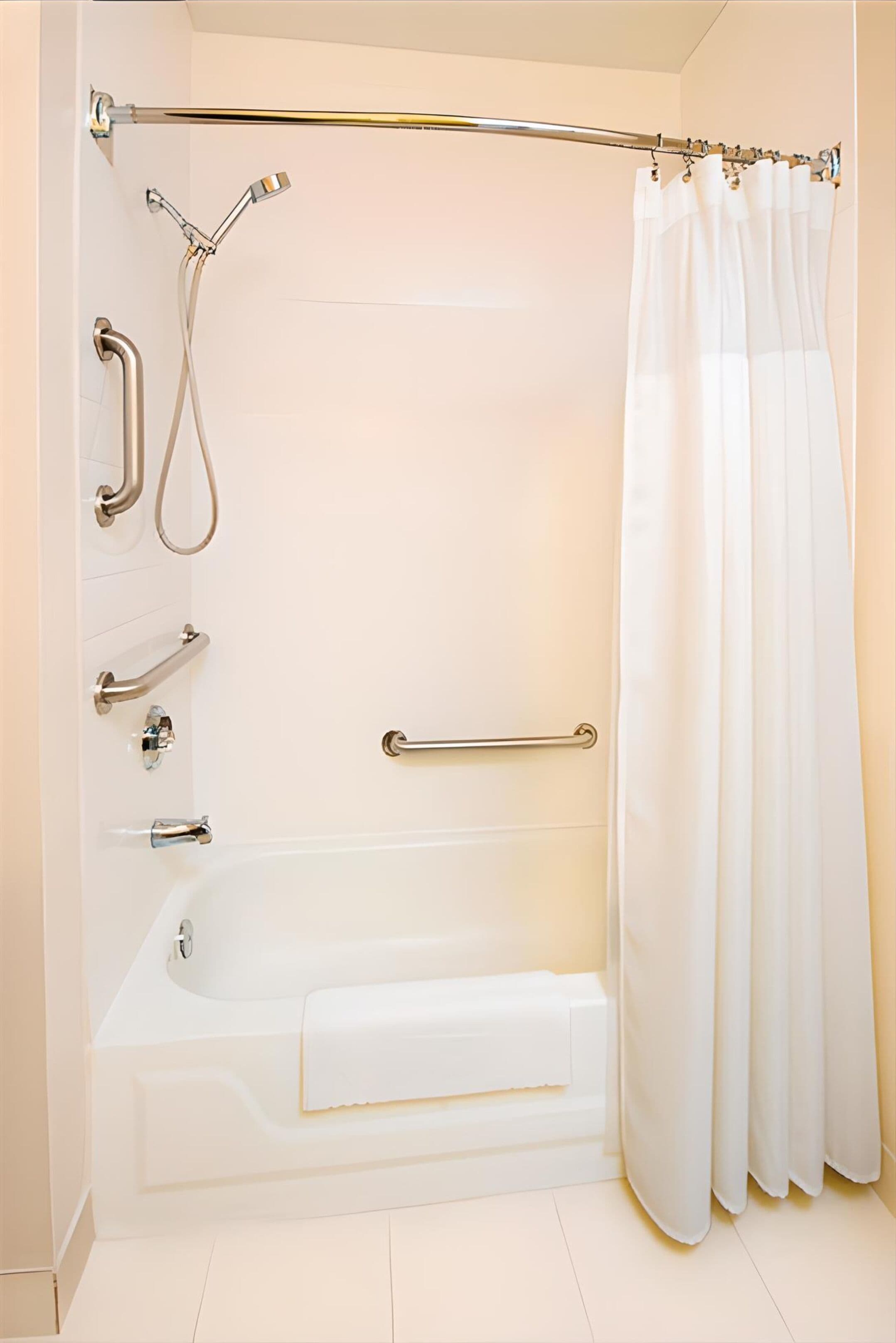 Une salle de bain moderne équipée d’une baignoire, d’une douche et de barres d’appui.