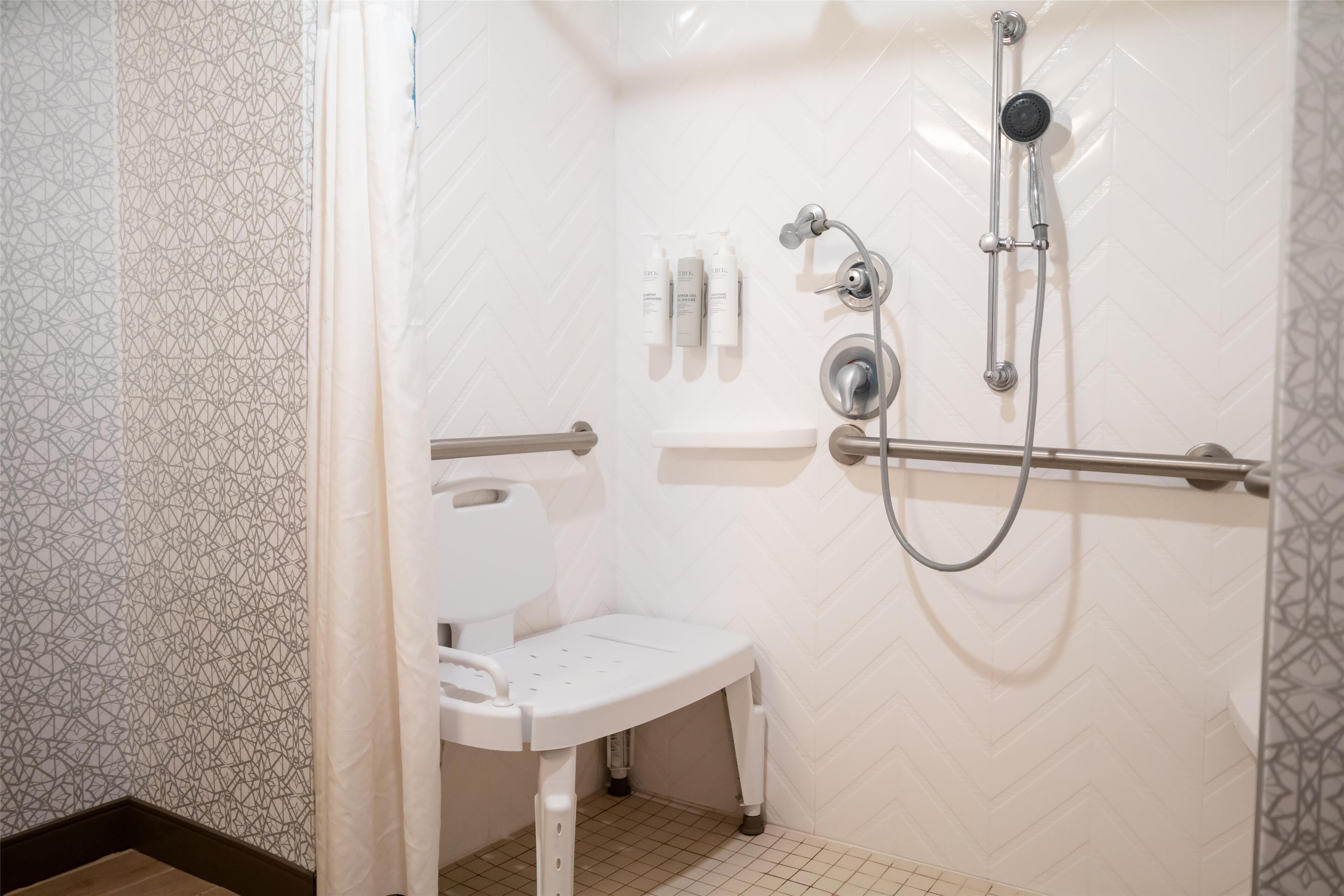 Un baño con ducha blanca, inodoro blanco y lavamanos blanco. Cuenta con un cabezal de ducha y un rociador de mano.