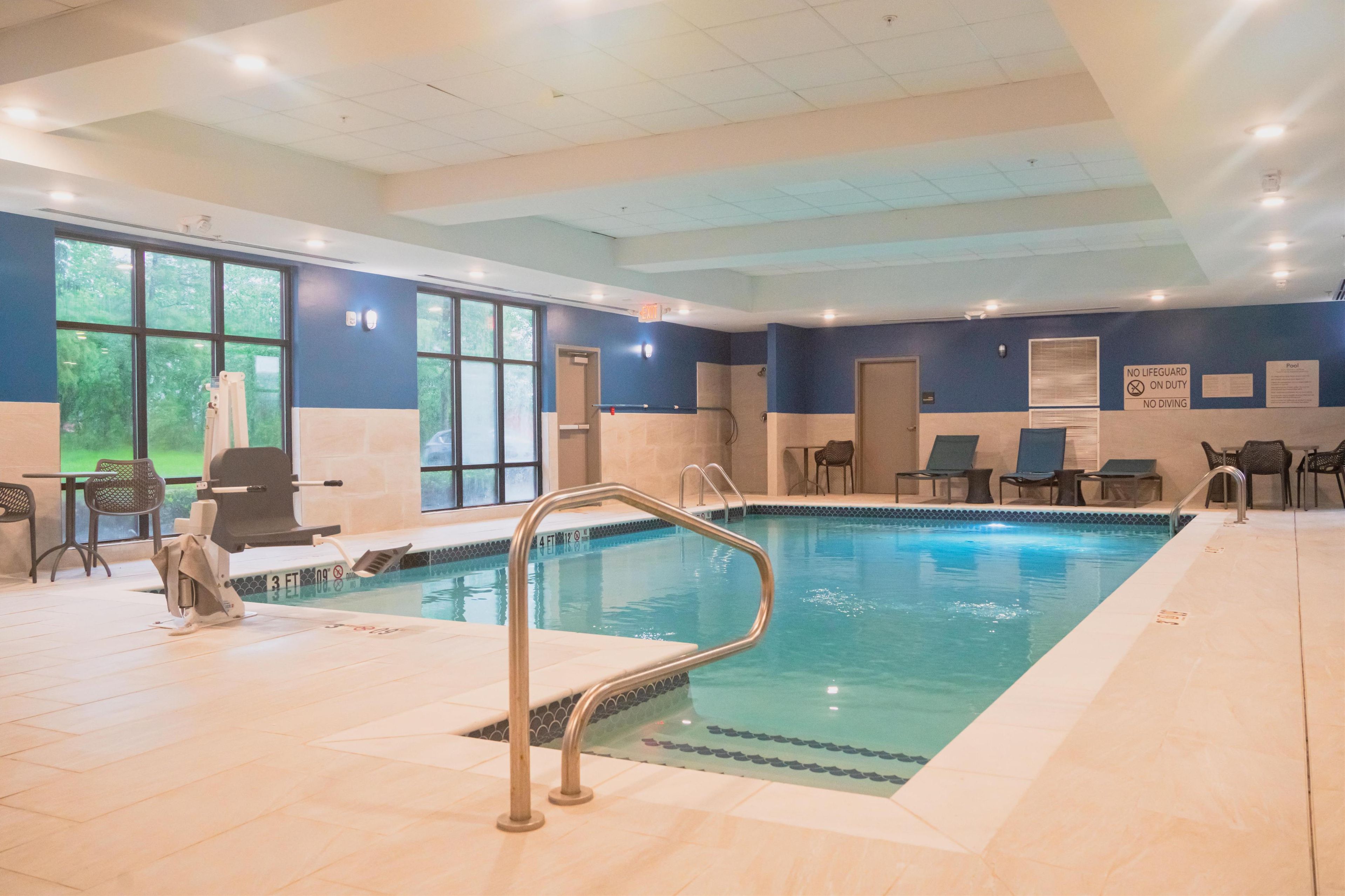 An indoor swimming pool with a lifeguard station, lounge chairs, and a view of the outdoors.