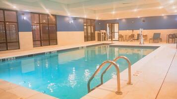 Una piscina interior con agua cristalina, suelo de baldosas y escalera de metal.