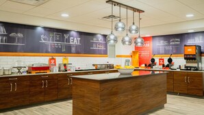 A modern kitchen with wooden cabinets, a central island, and a chalkboard wall with food-related drawings and text. - Hampton Inn Gonzales (Gonzales)