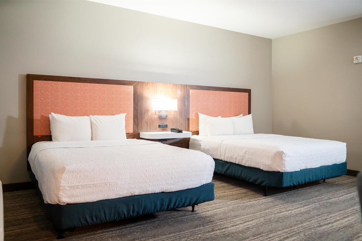 A hotel room with two beds, a nightstand, a lamp, and a wall-mounted mirror.