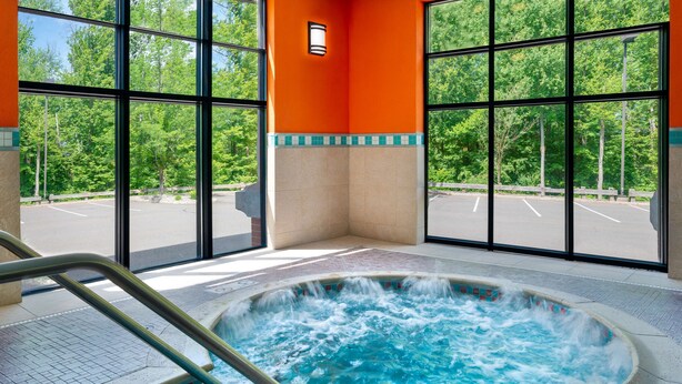 A hot tub with a tiled edge and a metal ladder, surrounded by large windows with a view of a parking lot and trees. - Hampton Inn Springfield South Enfield (Enfield)