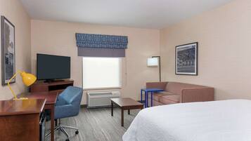 Ein Hotelzimmer mit Bett, Schreibtisch, Stuhl, Fernseher, Klimaanlage und einem Fenster mit Blick.