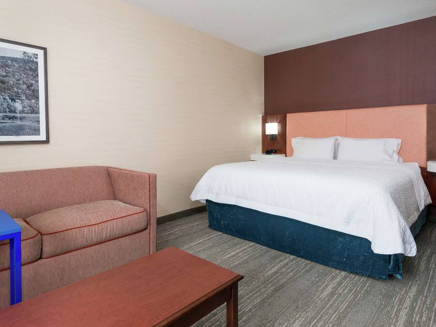 A hotel room with a bed, a sofa, a small table, and a framed picture on the wall.