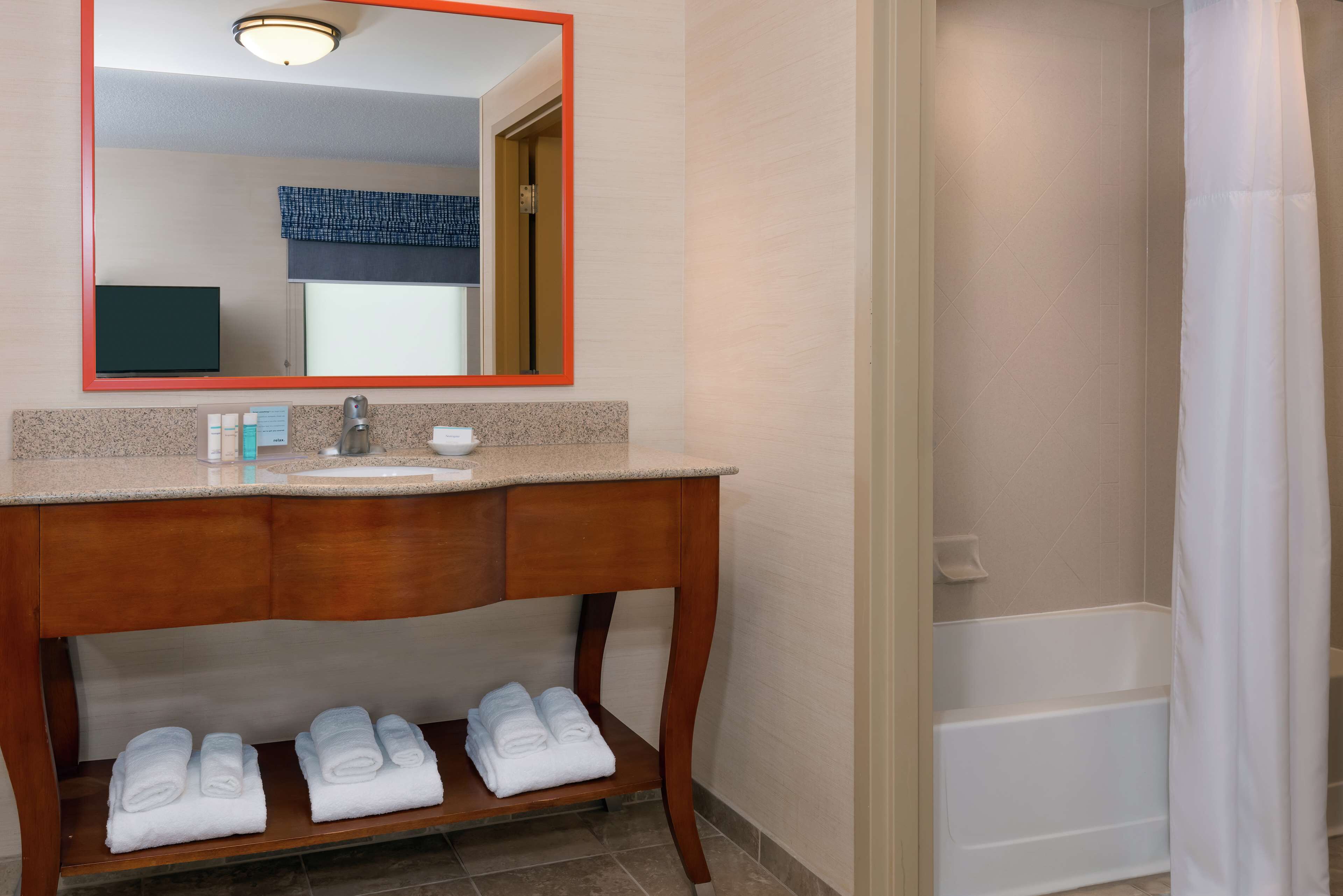 Een badkamer met een houten wastafelmeubel, een wastafel, een spiegel met oranje rand en een douchegedeelte.