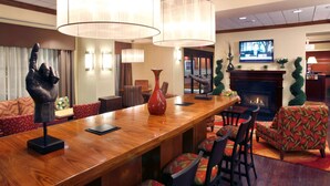 A hotel lobby with a wooden reception desk, comfortable seating, a fireplace, and a television. - Hampton Inn Springfield South Enfield (Enfield)